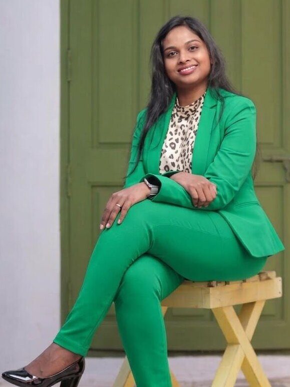 Ramya Sriramulu sitting on a yellow stool in front of a green door